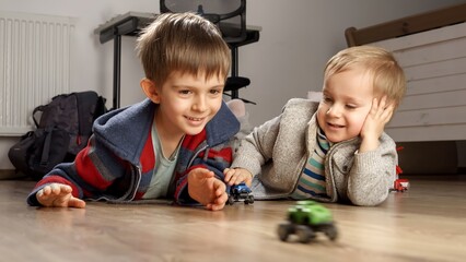 Portrait of two little boys playing with toys on wooden floor in bedroom. Children playing alone,...