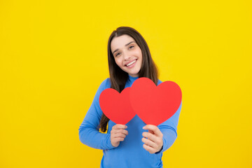 Fototapeta na wymiar Portrait of lovely sweet cute pretty girl hold red paper card heart isolated over yellow background. Beautiful girl holding heart, love shape.
