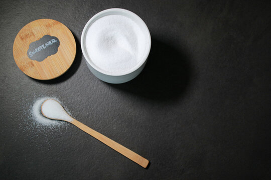 Natural sweetener in a white bowl with a wooden spoon, dark grey marble table