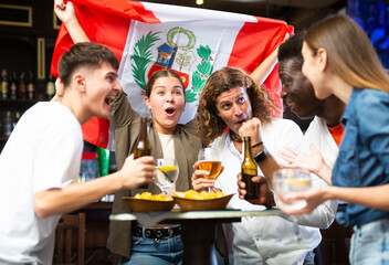 Multiracial Peru sports fans, men and women, supporting their favourite team in bar, raising state...