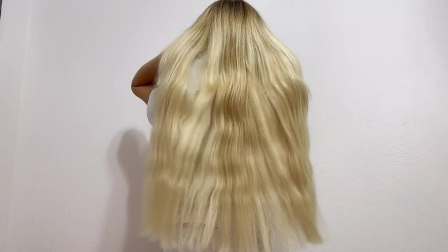A young blonde straightens her long straight hair with her hands on a white background. Professional hair extensions. Nice long hair. Female beauty with luxurious straight white hair.Sexy blonde model