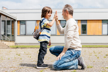 Dad and son say goodbye or meet after school near the school and give five to each other