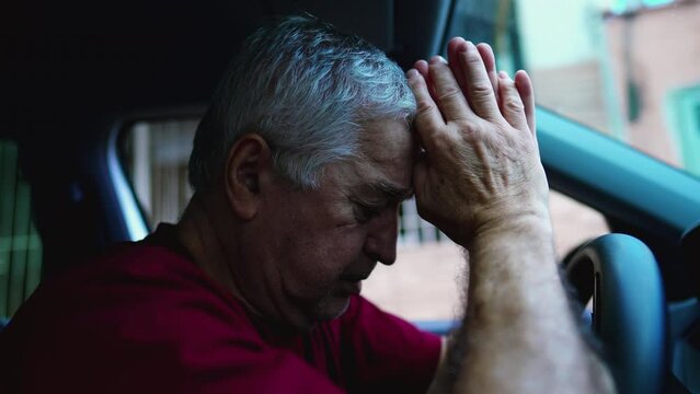 Religious senior man Praying to God during difficult times while sitting inside vehicle, parked in street looking at sky asking for divine help