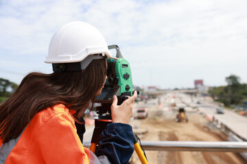 Site female  engineer operating her instrument during roadworks. Builder using total positioning station tachymeter on construction site for new road setting out