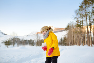 Preteen boy having fun playing with ice or snowball in forest among mountain valley on sunny day. Active winter outdoors leisure for family with kids. Travel in Lovcen National park
