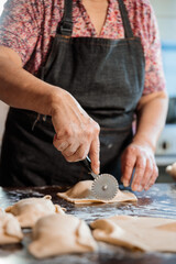 Unrecognizable Latin Elderly Woman using dough cutter knife for Preparing Chilean Beef Empanadas in Her Home Kitchen