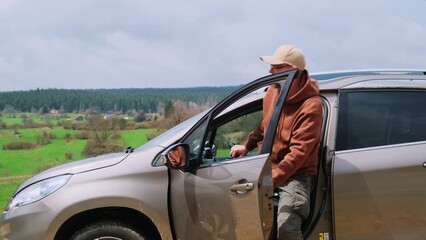 Adult man driver opens the door and gets out of the car on a country road.