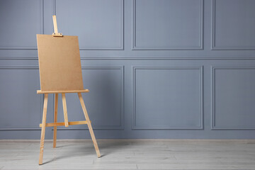 Wooden easel with blank board near grey wall indoors. Space for text
