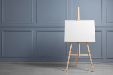 Wooden easel with blank canvas near grey wall indoors. Space for text - obrazy, fototapety, plakaty