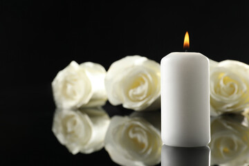 Fototapeta na wymiar White roses and burning candle on black mirror surface in darkness, closeup with space for text. Funeral symbols