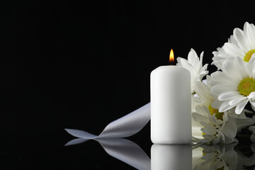 White chrysanthemum flowers and burning candle on black mirror surface in darkness, space for text....