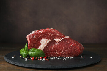 Fresh raw cut beef, spices and basil leaves on wooden table