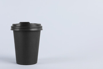 Black paper cup with plastic lid on light background, space for text. Coffee to go