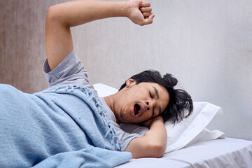 Portrait of yawning man stretching his arms while still on his bed