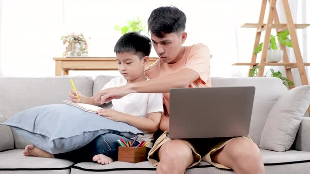 Fatherhood multitask lifestyles concept, father in casual working on laptop taking care adorable son, father spending time playing with kid at home, cute Asian boy sit close to dad painting on paper
