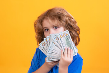 Child with lots of money dollar banknotes isolated over yellow studio background.