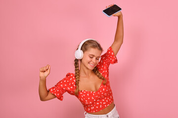 Young happy energetic Caucasian woman teen dancing holding phone in hands and listening to music in...