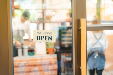 Hand of coffee shop staff woman wearing apron turning open sign board on glass door in modern cafe,...