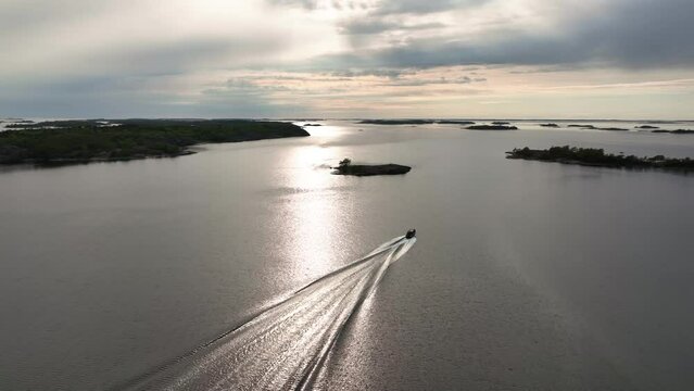 Aerial view following a boat driving in the archipelago of Saaristomeri, cloudy evening in Finland