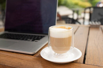 Coffee cup on the table in coffee shop as blur laptop background.
