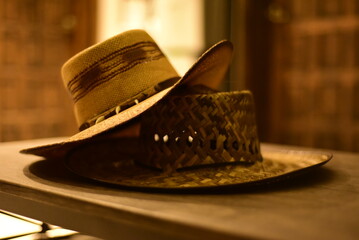 Sombreros amigables.  Sombrero de paja rijida tostada con colmillos encima de sombrero de paja cosido, sobre mesa de madera. Primer plano.