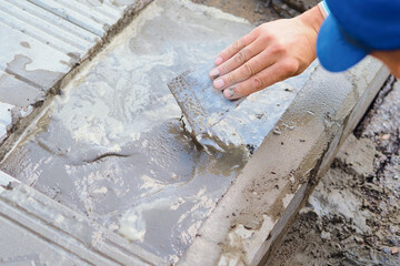 Builder grouts tiles on foundation of building with cement. Blind area repair. Bricklayer laying tiles. Hand of worker with trowel close-up.
