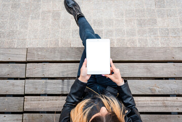 Mockup image of woman holding and using white tablet pc with blank white desktop screen while sitting on the wooden bench.Top view.Copy space.