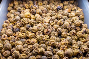 Dried black pepper in a food container close-up