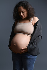 Beautiful woman in a blazer and jeans, touches her pregnant belly in the ninth month of her happy...