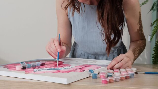 Painting by numbers. Woman drawing picture by numbers with acrylic paints on canvas at home. Painting on canvas for beginners. Creative hobby. Selective focus.