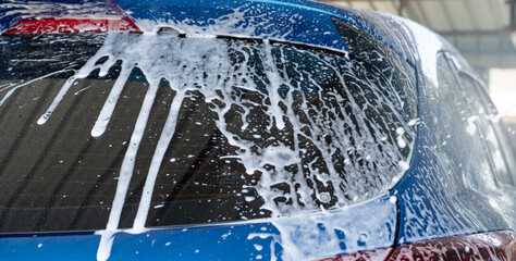 Blue car wash with white soap foam and professional auto care service. Car cleaning service...