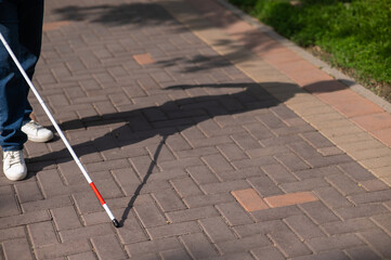 A faceless blind woman walks down the street with a cane. 
