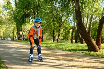 Little preteen boy wearing protective gear and helmet roller skating in park