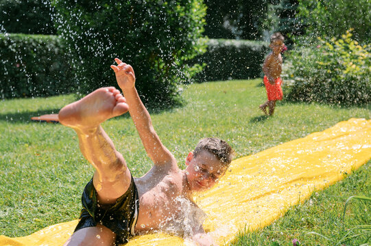 Kids Having Fun On Water Slide In Garden