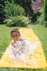 A boy plays outside on a water slip and slide