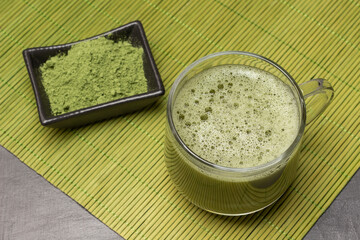 Matcha tea in a glass, matcha tea powder in a black bowl on a green bamboo napkin.