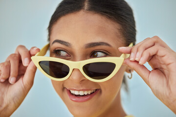 Smile, sunglasses and young woman in a studio with a casual, stylish and cool eyewear. Happy, excited and female model with trendy gen z style and fashion accessory isolated by a blue background.