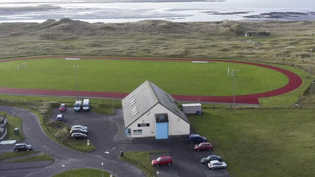 Dynamic, drone shot circumnavigating the Dark Island Hotel near a track and football pitch. Filmed in Linaclate on the Isle of Benbecula, part of the Outer Hebrides of Scotland.