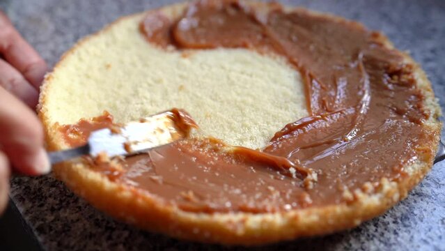 Person Spreading Caramel On Round Sponge Cake. - closeup
