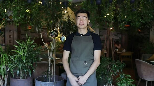 Handsome waiter guy welcoming customers into the restaurant. Smiling server inviting guests with gesture into cafe. Millennials at work. Fine dining restaurant concept.