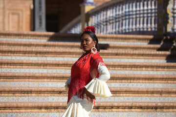 Young black woman dancing flamenco in a square in Seville, Spain. She wears a beige dress with...