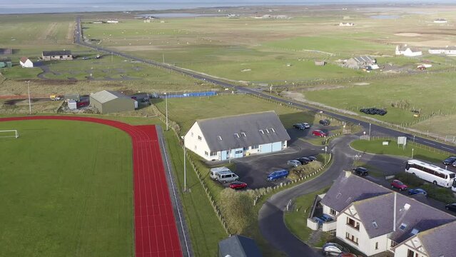 Drone shot circumnavigating the UHI college campus on the Isle of Benbecula. A track and football pitch is visible, as well as the distant sea. Filmed in Linaclate, part of the Outer Hebrides.