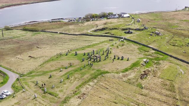 Drone shot dollying forward of the Callanish Standing Stones on the Isle of Lewis, part of the Outer Hebrides of Scotland. Filmed on a sunny, summers day. Tourists and visitors are visible.