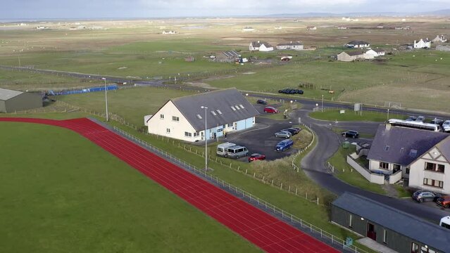 Drone shot of the UHI college campus on the Isle of Benbecula near the Dark Island Hotel. A track and football pitch is visible, as well as a nearby crofting farm. Filmed on the Outer Hebrides.