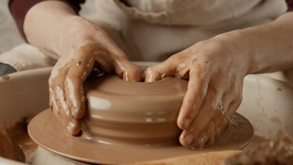 Potter making ceramic plate or dish on pottery wheel. Two hands create bowl. Potter shapes clay product. Close-up in 4K, UHD