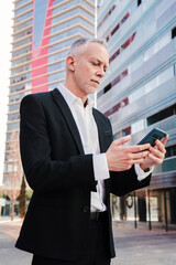 Vertical. Middle aged businessman using a smartphone to check his stock shares. Well dressed...