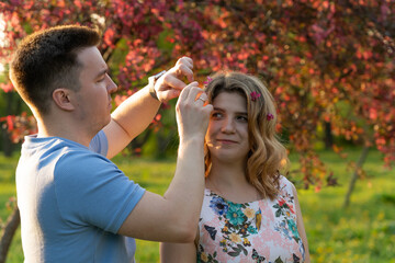 guy adorns girl's hair with blossoming apple tree flowers. young couple in an apple orchard at sunset, during golden hour. photo captures essence of romantic date, tenderness, heartfelt attention.