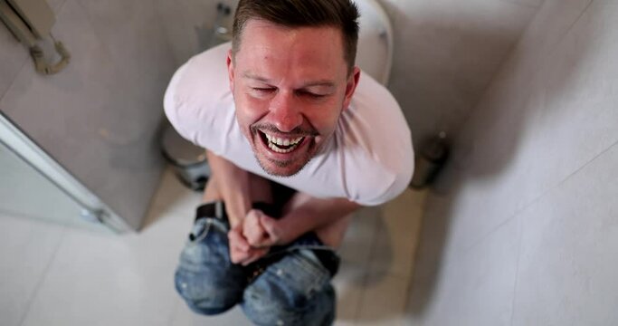Young man sitting on toilet and screaming in pain during bowel movements 4k movie slow motion. Constipation as cause of hemorrhoids concept