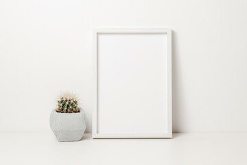 Photo frame mockup with cactus in pot on white wooden table. Photo frame template with copy space for design, poster or picture, aesthetic home decoration, cozy scandinavian style