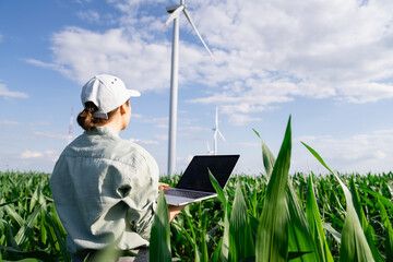 Agronomist examining plants and standing with laptop on sunny day at field
